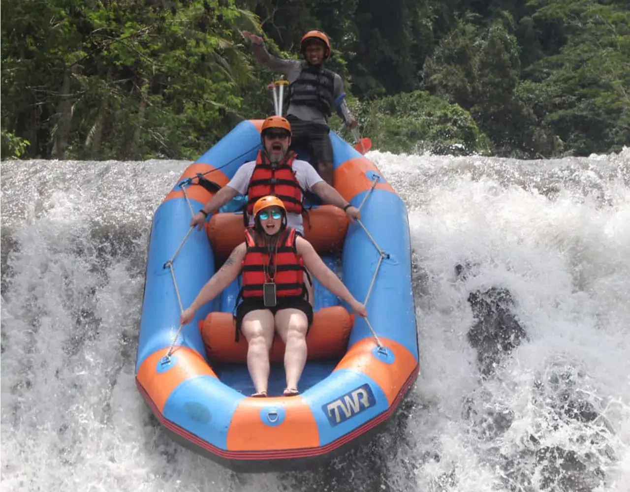A blue and orange raft sliding down the dam drop with the guide standing at the back
